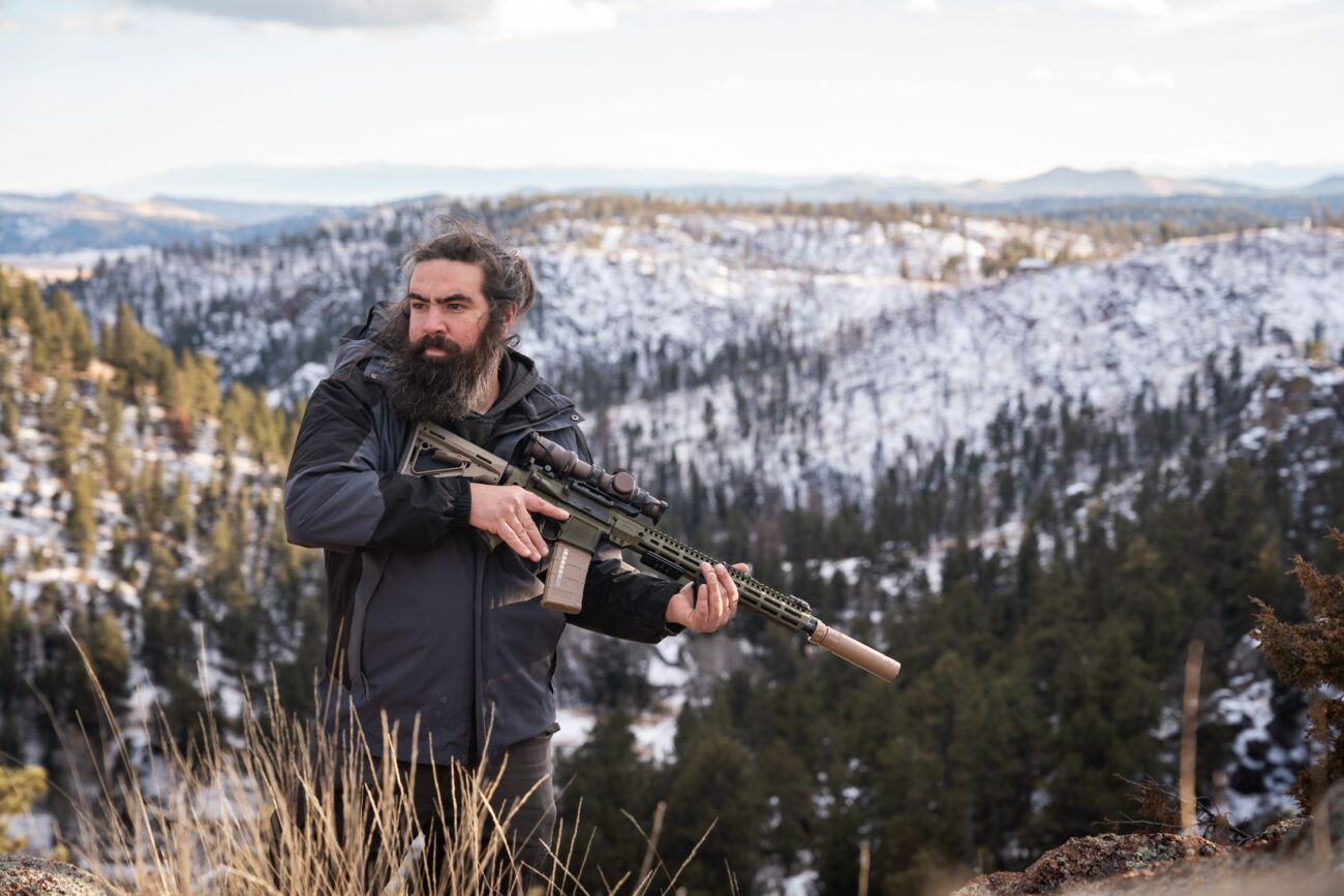 Guy standing with his firearm with the view of a mountain behind him.